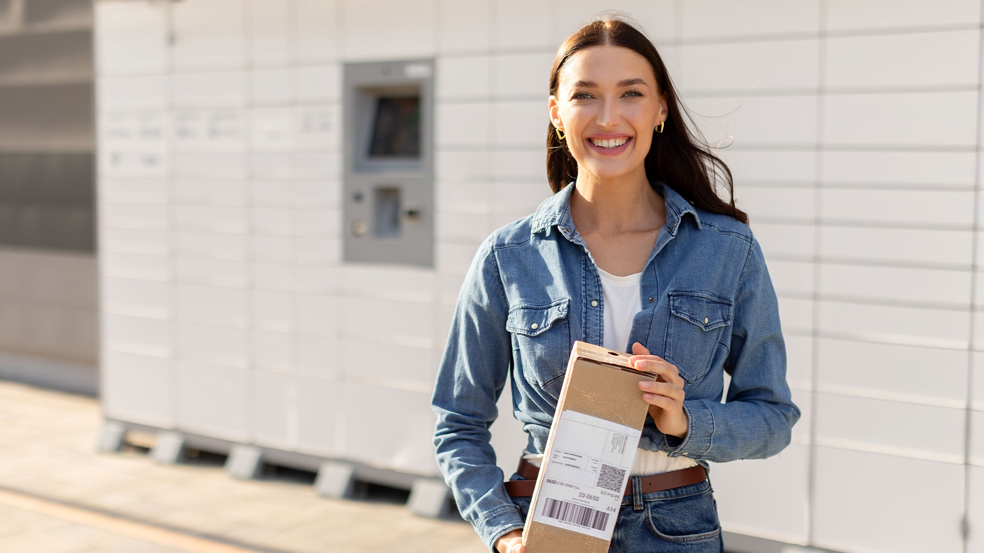 Woman smiling holding a package standing in front of parcel smart locker